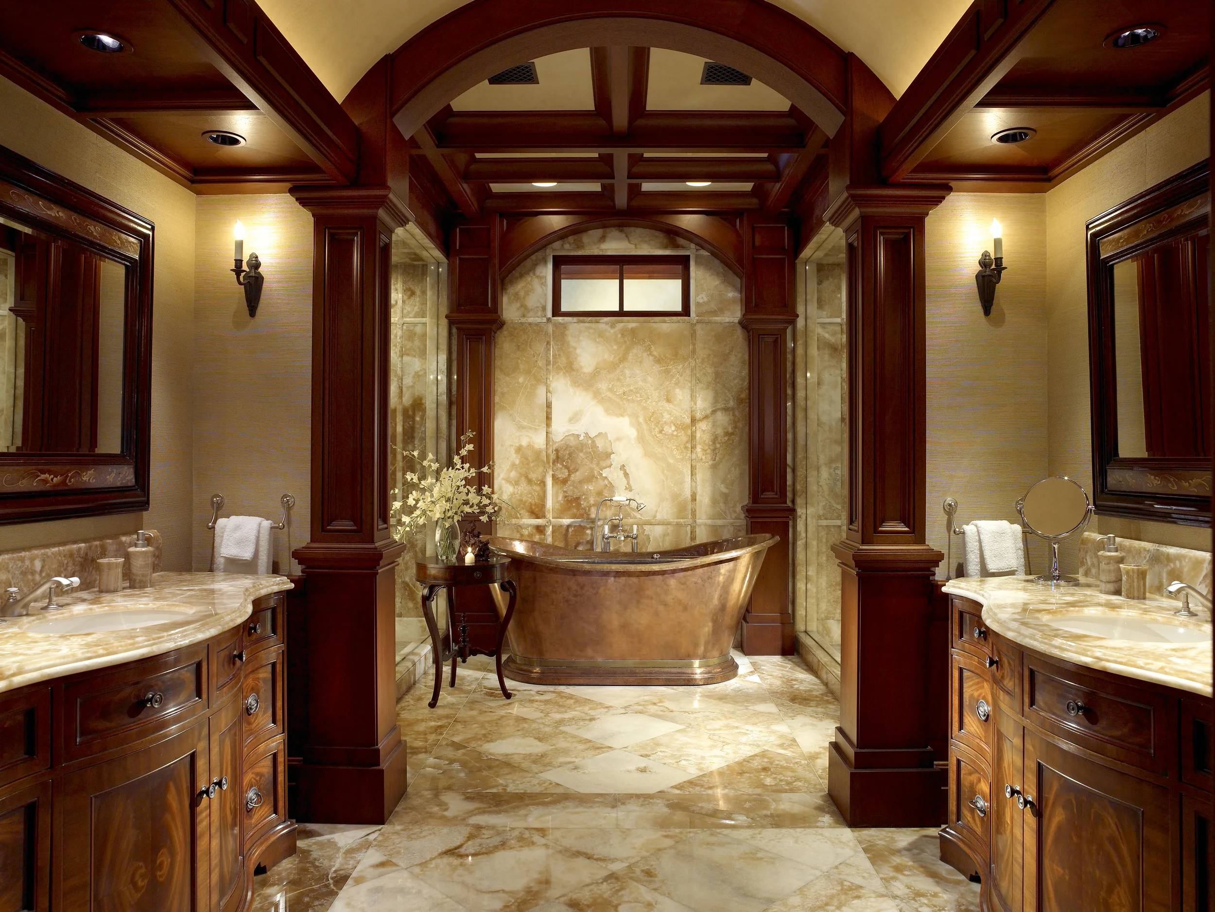 Symmetrical private bathroom featuring custom wood cabinetry, stone surfaces, architectural paneling, and a freestanding copper-toned bath.